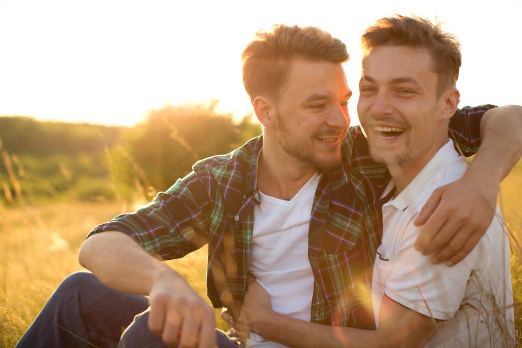 Men laughing and hugging in field at sunset